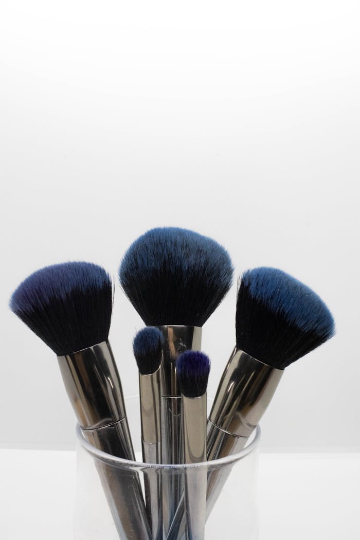 Collection of blue-tipped makeup brushes elegantly arranged in a clear glass holder.