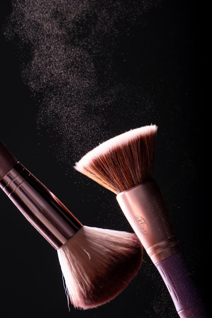 Close-up of makeup brushes with powder on black background, capturing dynamic movement.
