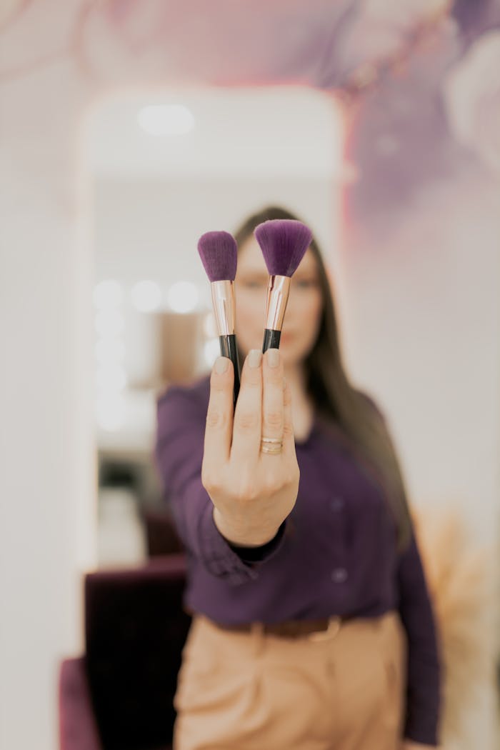 A woman holds two makeup brushes, symbolizing beauty and fashion.